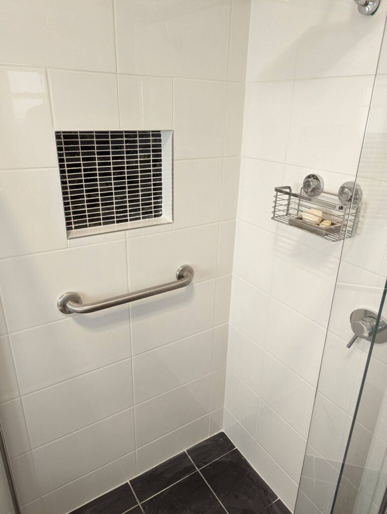 white and beige shower wall tiles with light grout and a handheld showerhead.