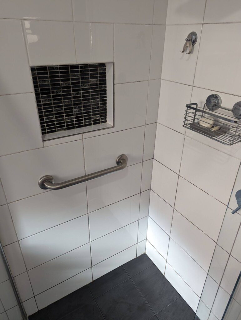 discoloured grout on white shower tiles around a black mosaic niche.